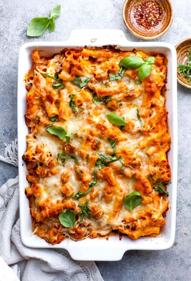 Baked Ziti in white baking dish with cheese and fresh basil. 