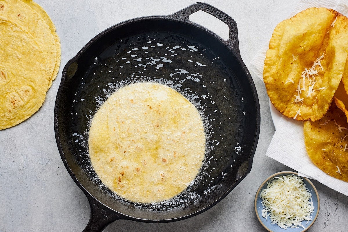 tortilla being fried in oil in cast iron skillet to make crispy taco shells.