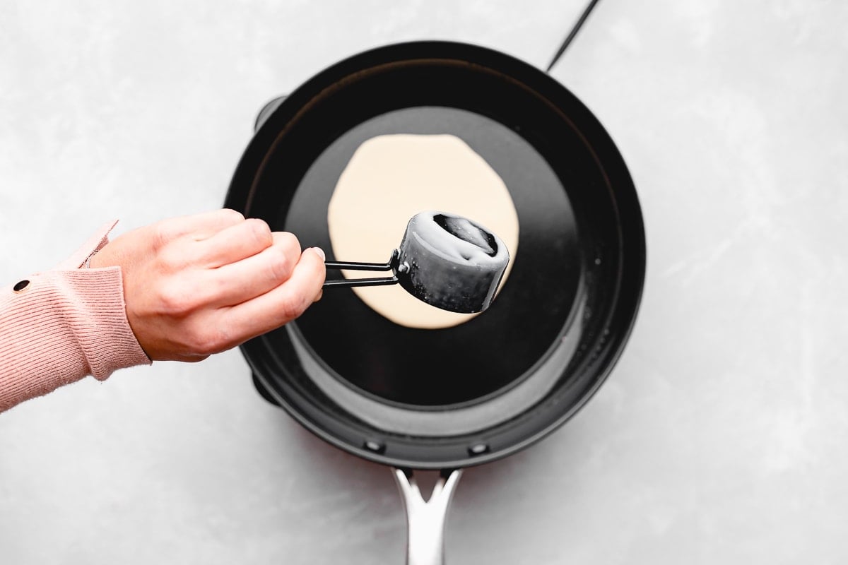 crepe batter being poured into a skillet with a measuring cup.
