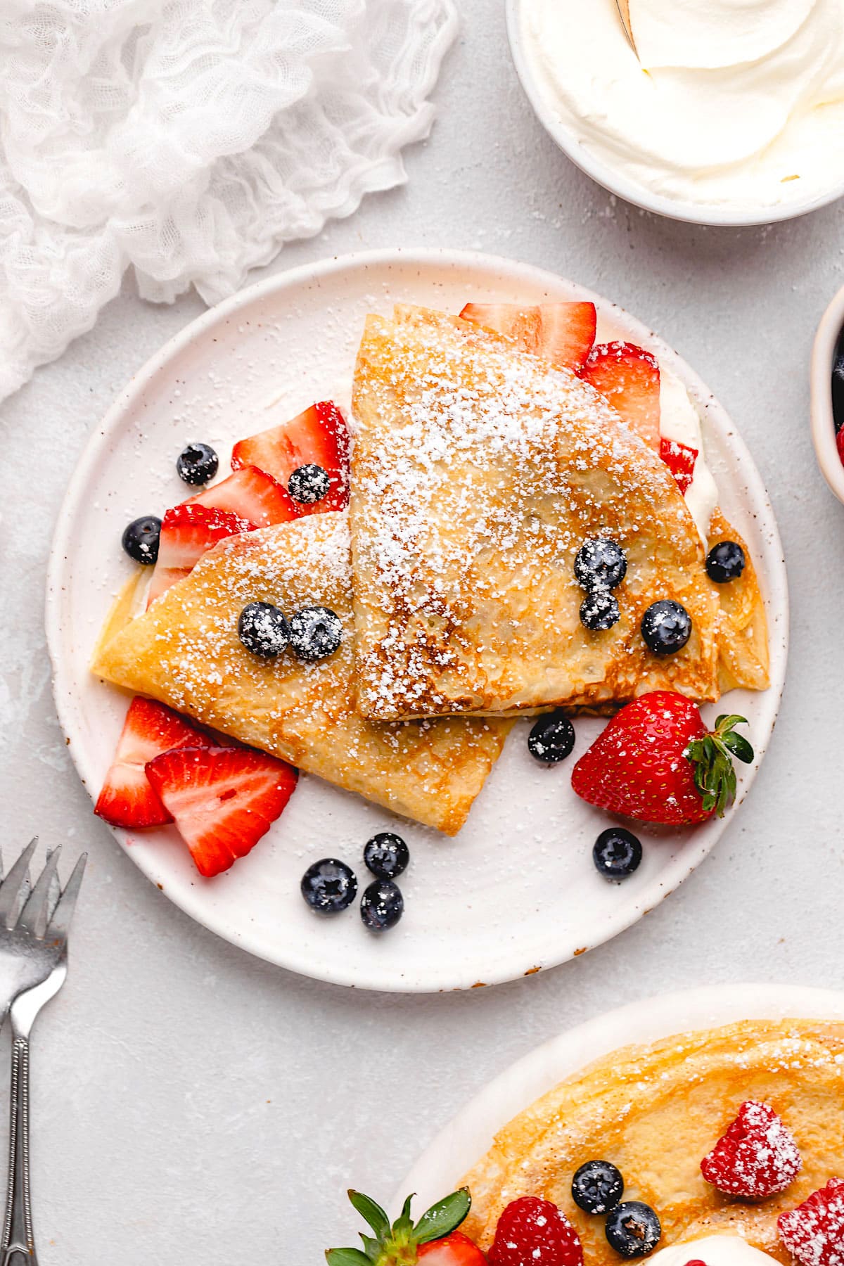 crepes folded on plate with berries and powdered sugar.