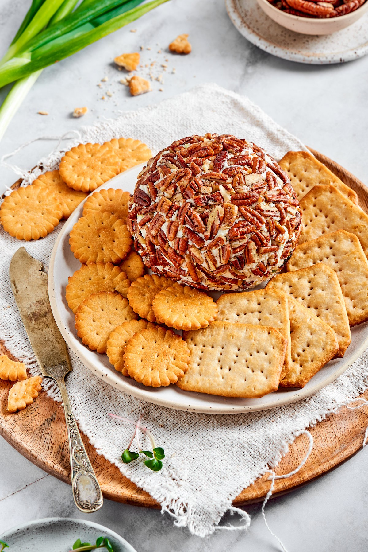 cheese ball covered in pecans on plate with crackers and knife on the side. 