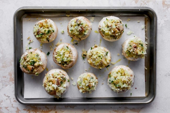 uncooked stuffed mushrooms on baking sheet with parchment paper.